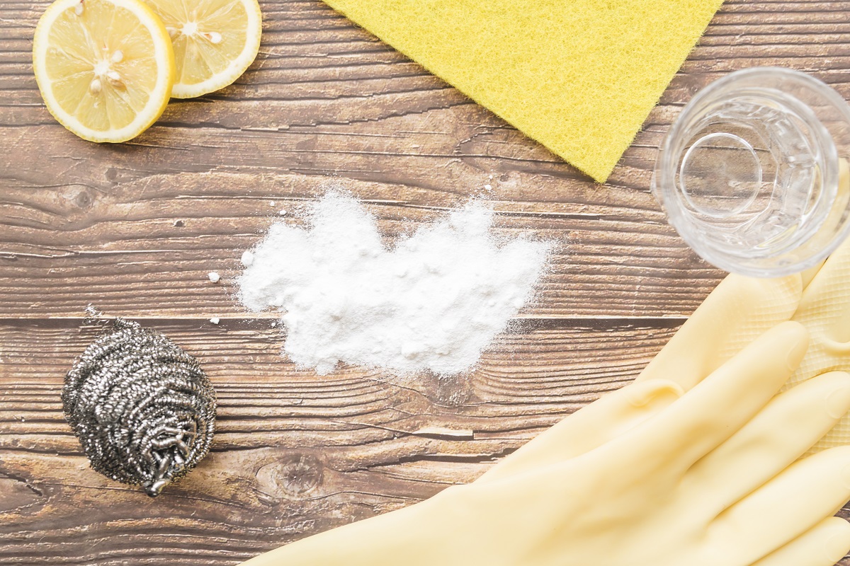 two lemon slices, baking soda, and a pair of yellow rubber gloves on a wooden surface