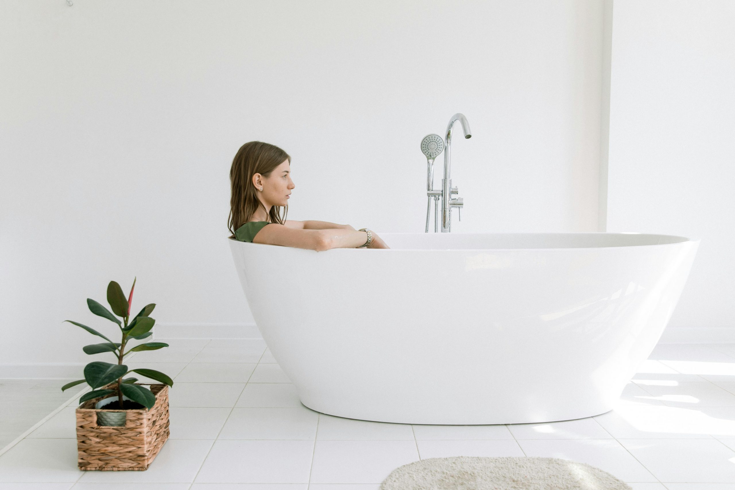 woman sitting in a white porcelain bathtub with an indoor plant placed nearby