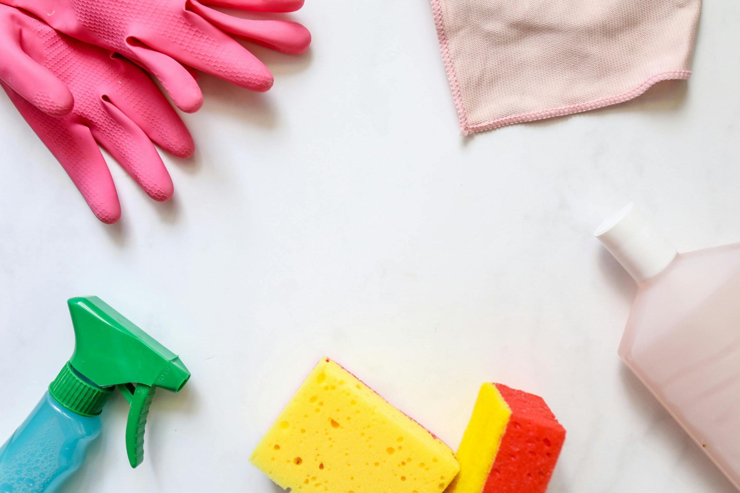 pink rubber gloves, yellow sponges, and a blue spray bottle on a clean white surface